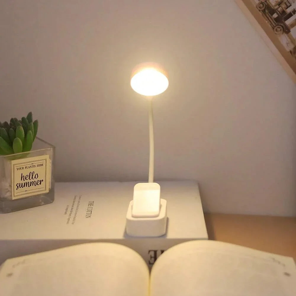 Mini white clip-on book light standing on a book next to a plant and open pages