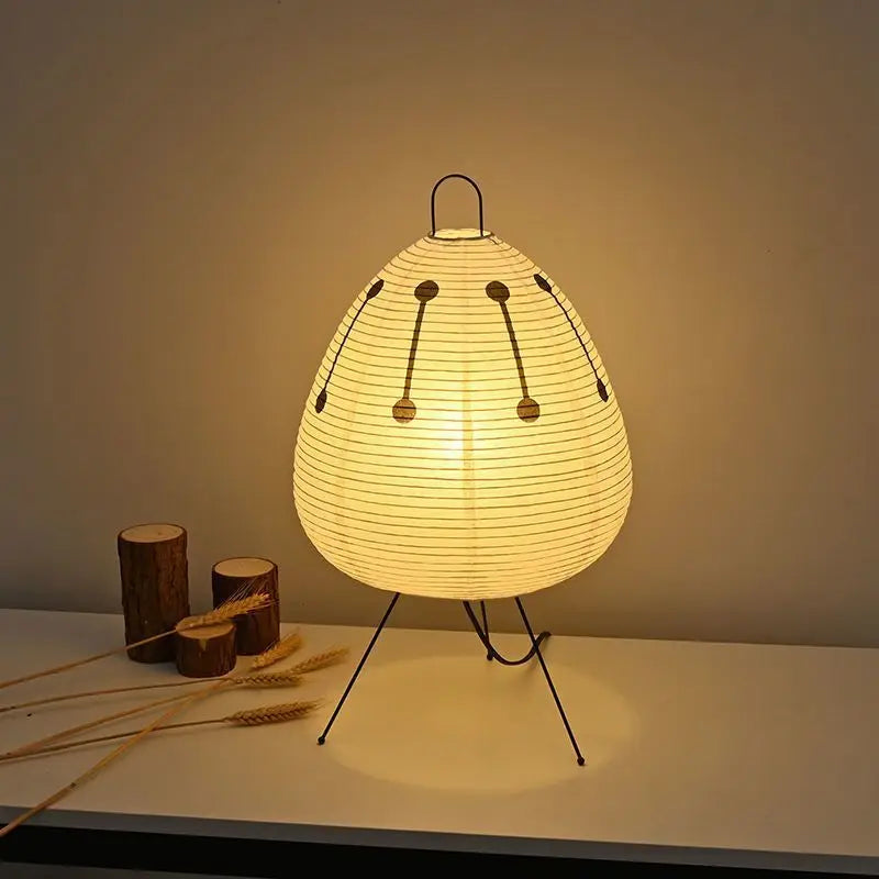 Minimalist rice paper table lamp lit and placed on a white console with decorative wood accents nearby