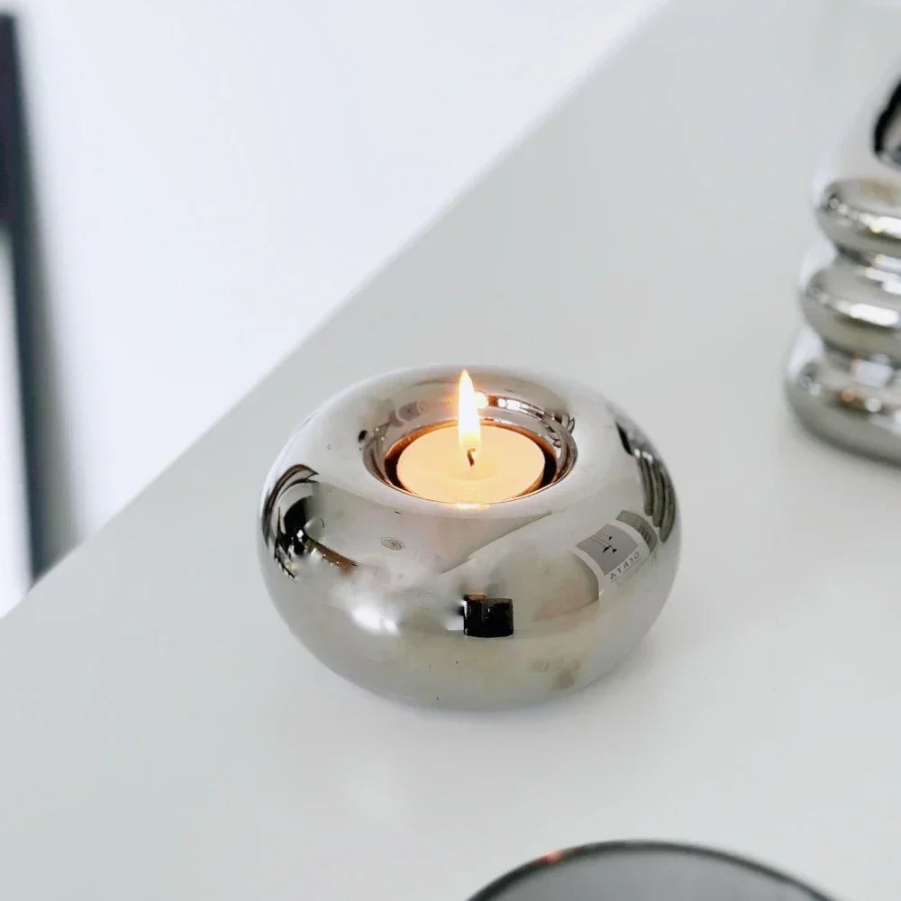 silvery ceramic tealight holder with a lit candle shown on a white tabletop