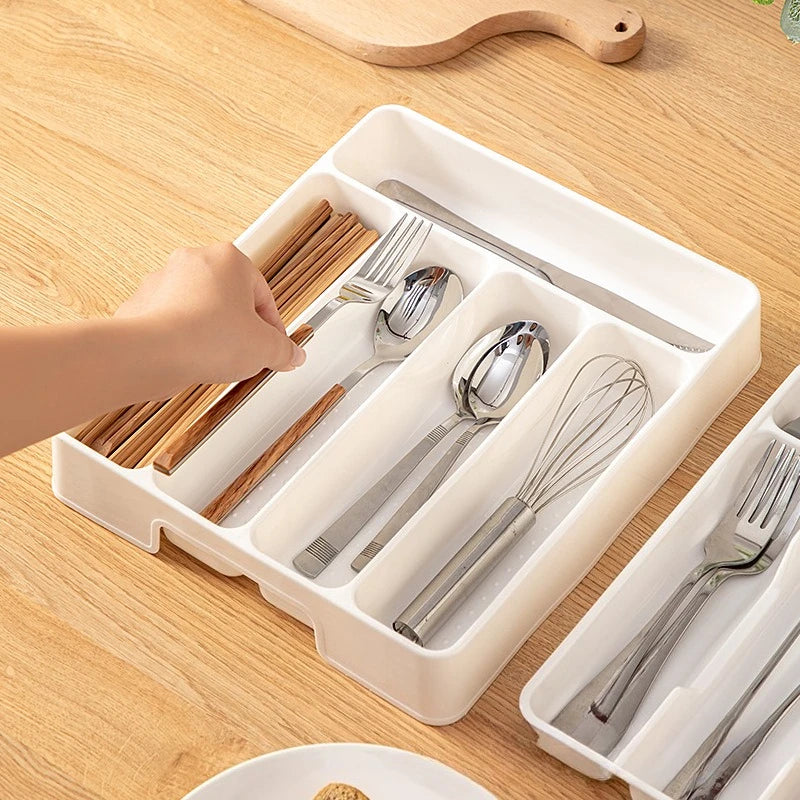 Hand selecting utensils from a white cutlery organizer tray on a wooden surface