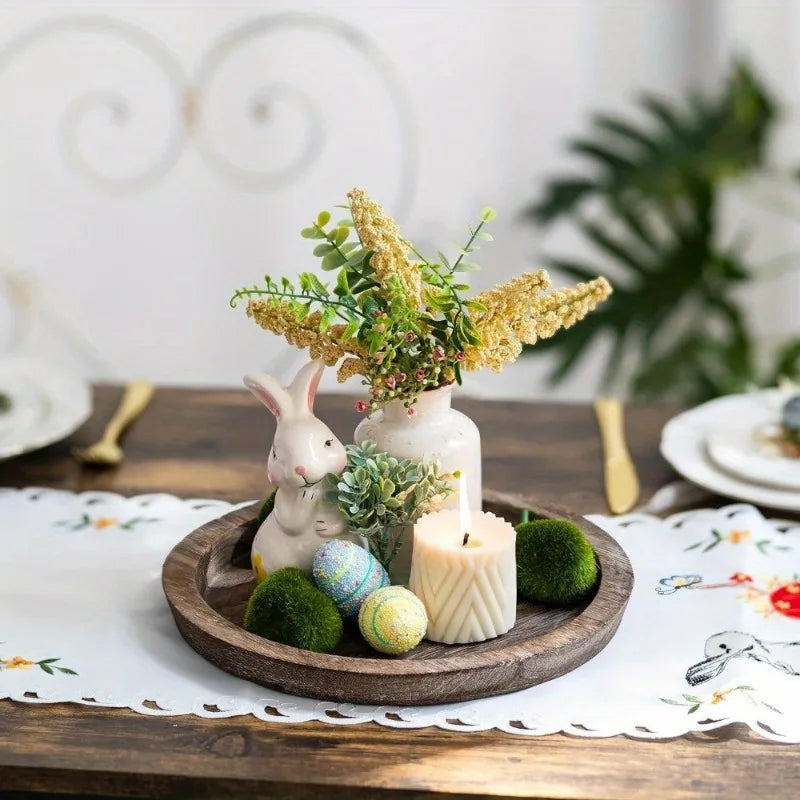 Round wooden tray used as a centerpiece with a vase, bunny figurine, candle, and decorative eggs on a dining table