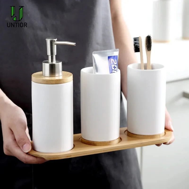White ceramic bathroom accessories set with soap dispenser, tumblers, and wood tray being held