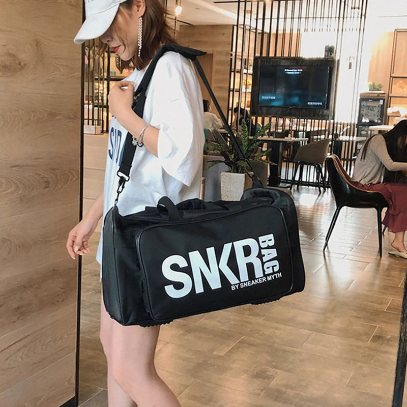 Person holding the SNKR BAG duffel bag by the shoulder strap inside a room