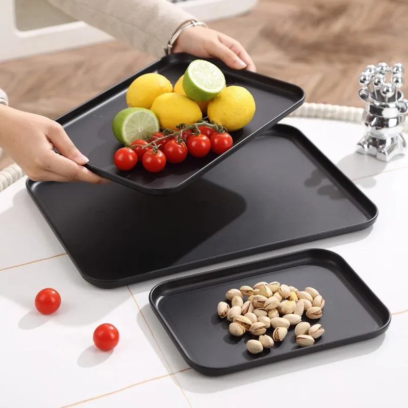Hands picking up a black tray with lemons, limes and tomatoes, other trays with snacks on a table