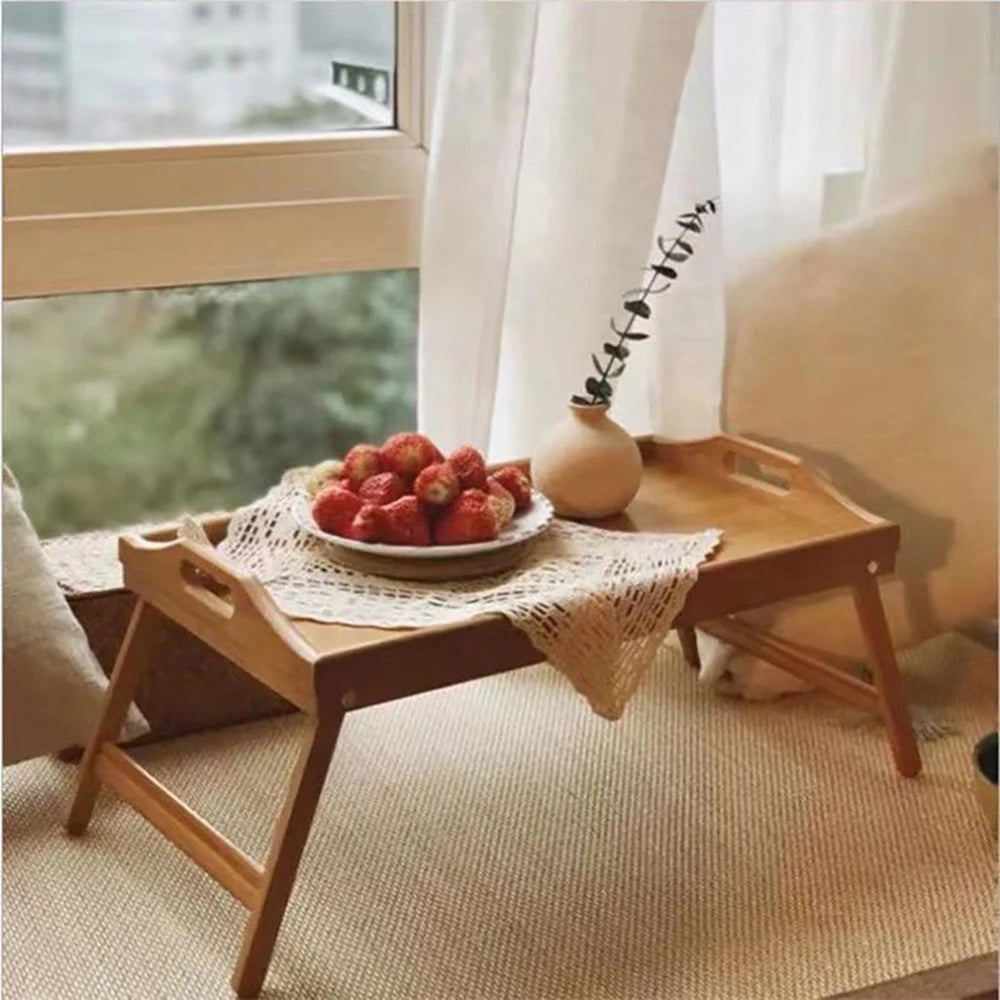 bamboo breakfast tray table with strawberries and a small vase by a window seat