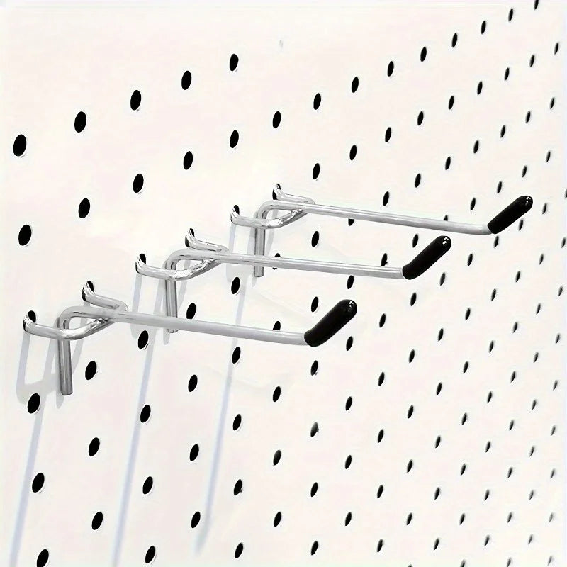 three metal pegboard hooks with black end caps installed on a white pegboard panel