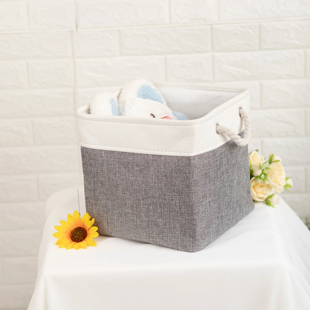 Gray fabric storage bin with white trim and rope handles, staged with flowers and a plush toy for home organization