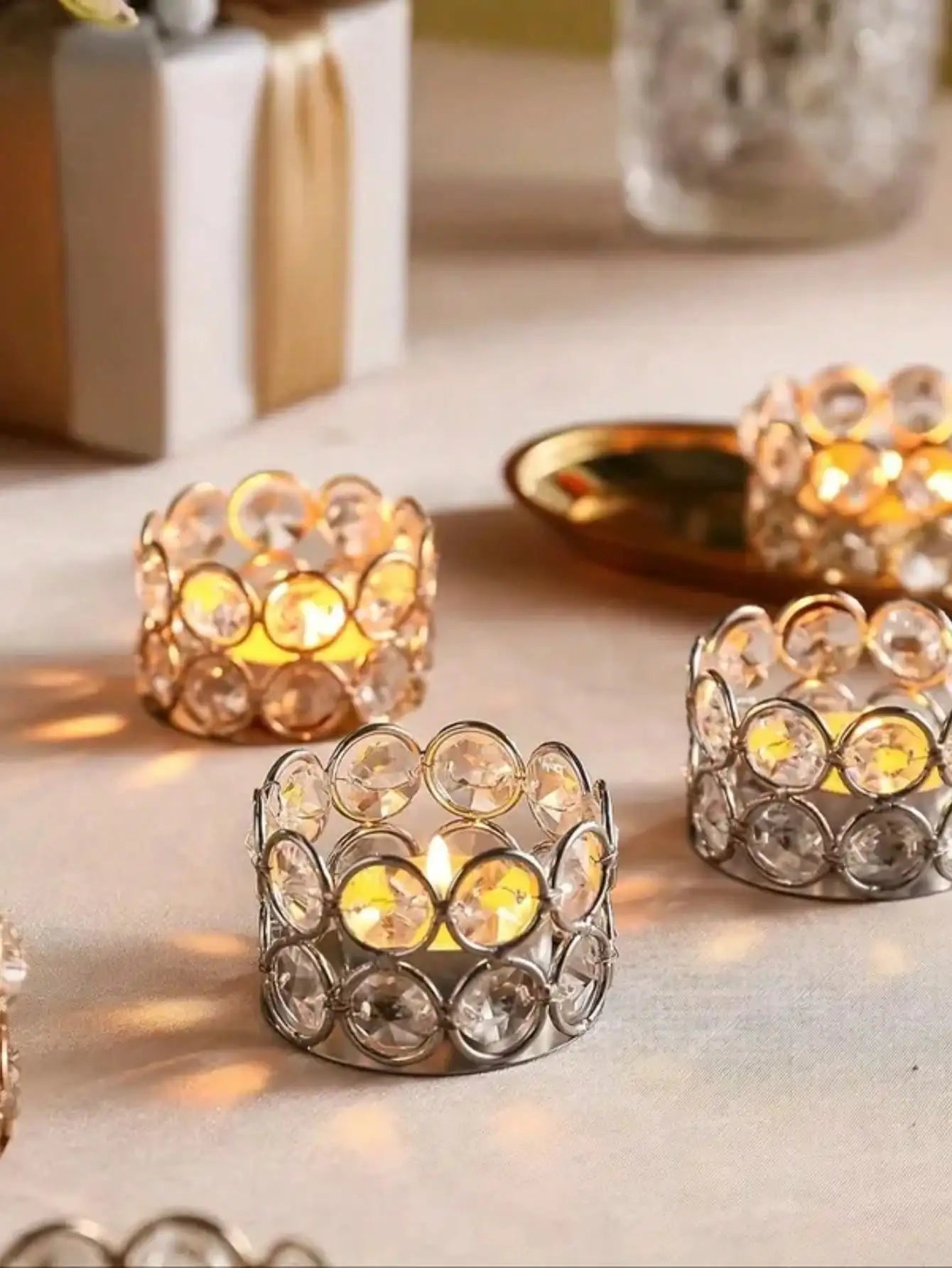 Crystal tealight holders in gold and silver on a tabletop, each holding a tealight candle