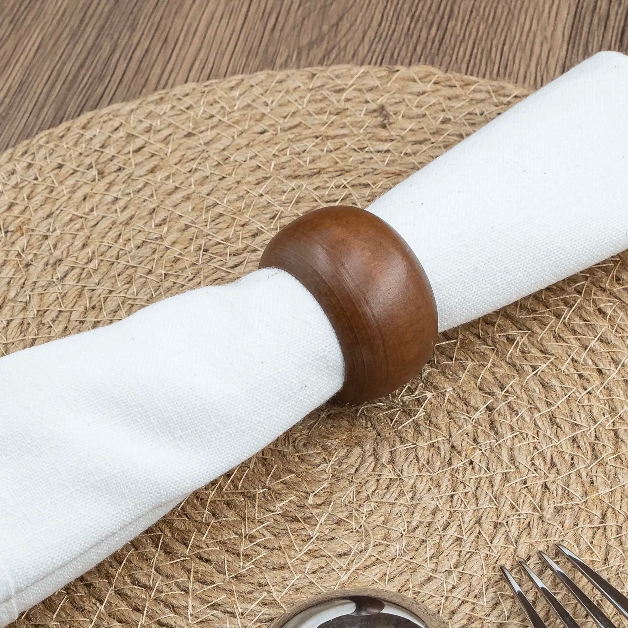 Closeup of acacia wood napkin ring holding a white cloth napkin on a woven placemat