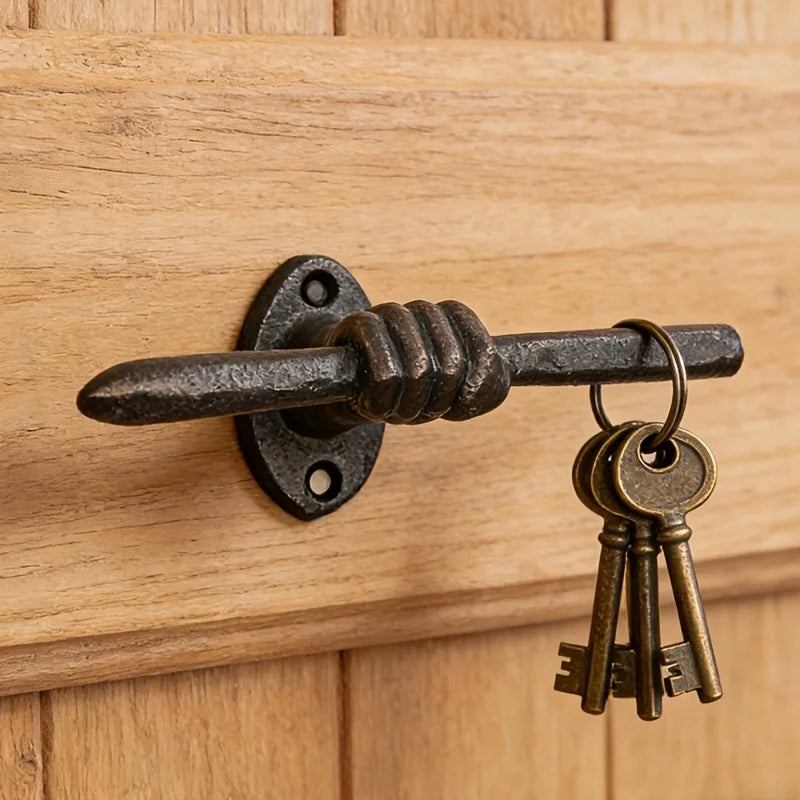 Cast iron wall hook shaped like a hand gripping a bar, mounted on wood, holding a set of keys