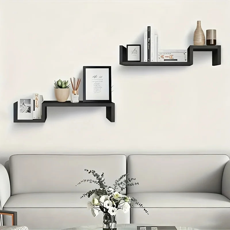 Two black S-shaped floating shelves used as book and decor display above a couch in a living room