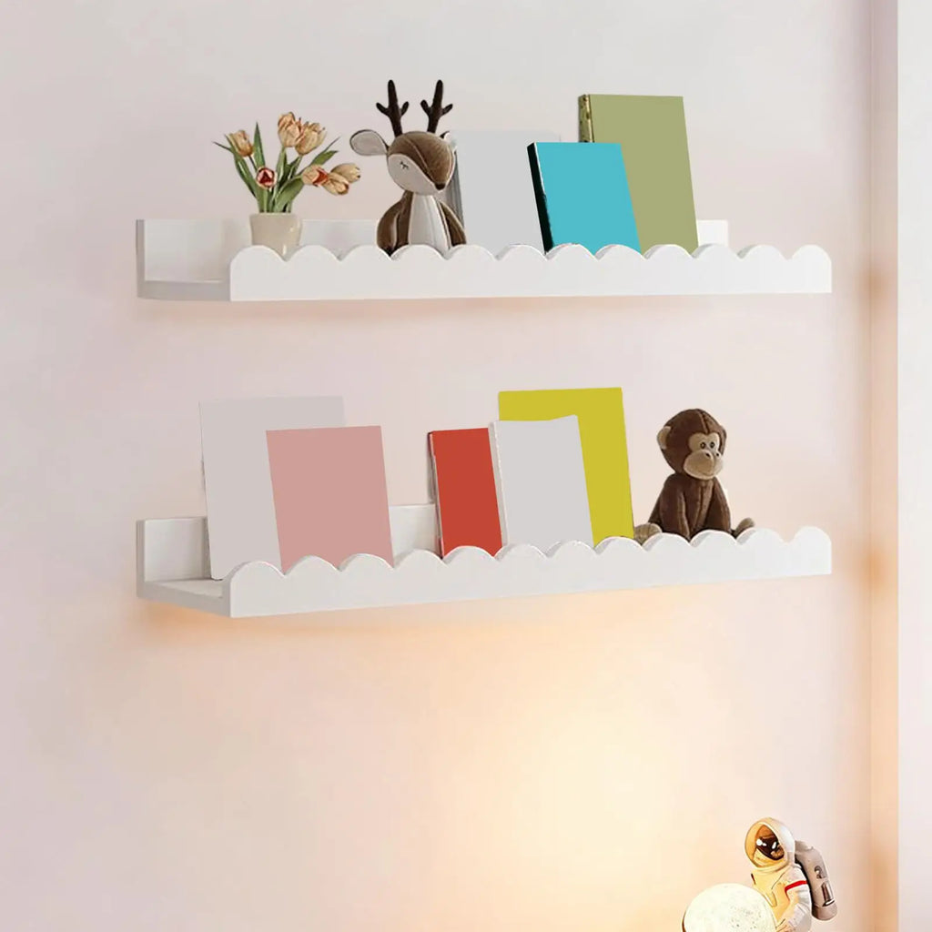 Two white scalloped-edge wooden wall bookshelves in a child's room, holding books, toys, and a small vase