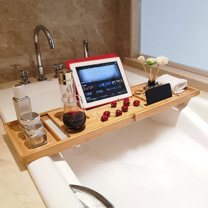 Extendable bamboo bath tray on a tub with wine, tablet, toiletries, and flowers organized.