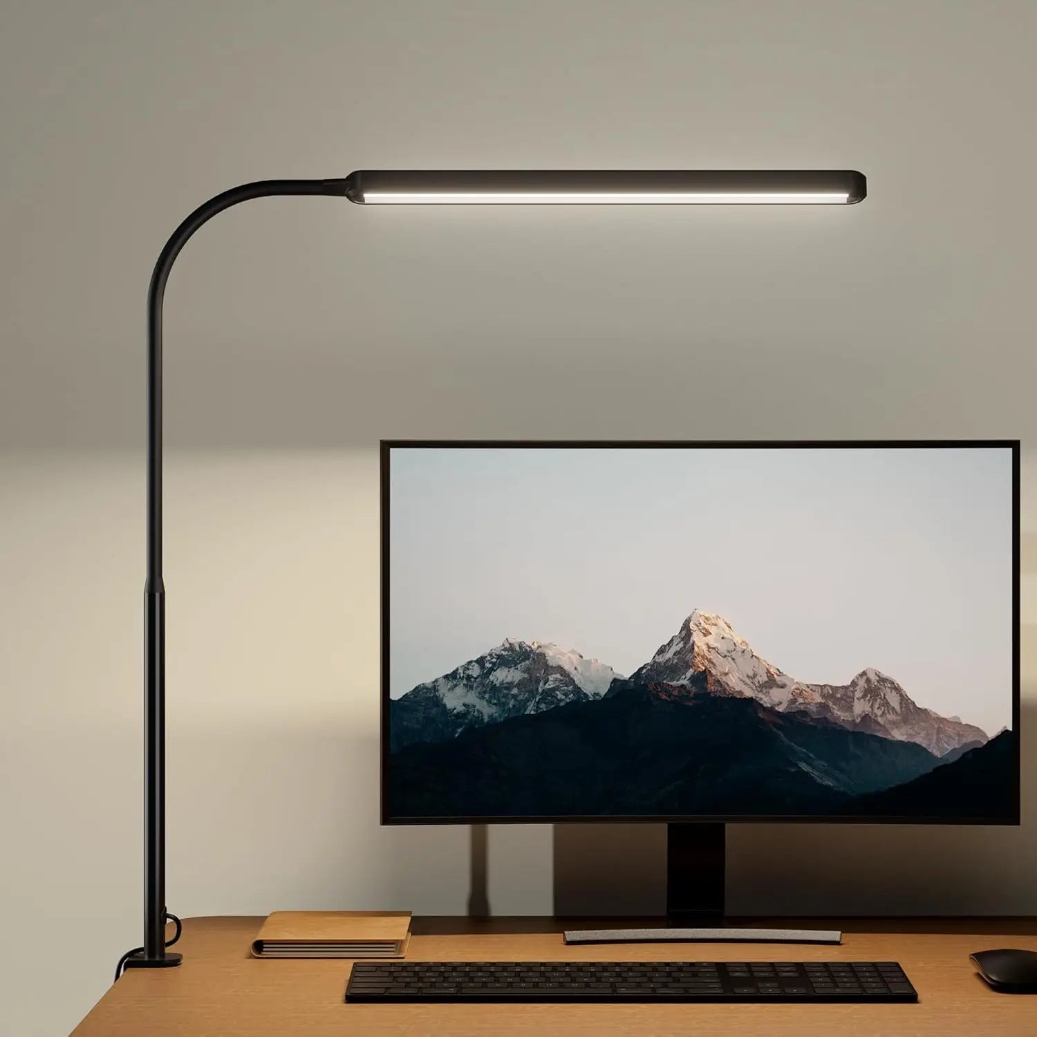 Black clamp-on LED desk lamp with a long gooseneck positioned above a computer monitor