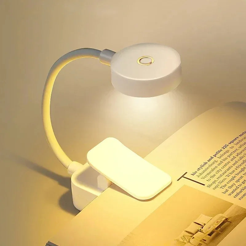 White portable LED reading light clipped onto open book with a soft warm glow