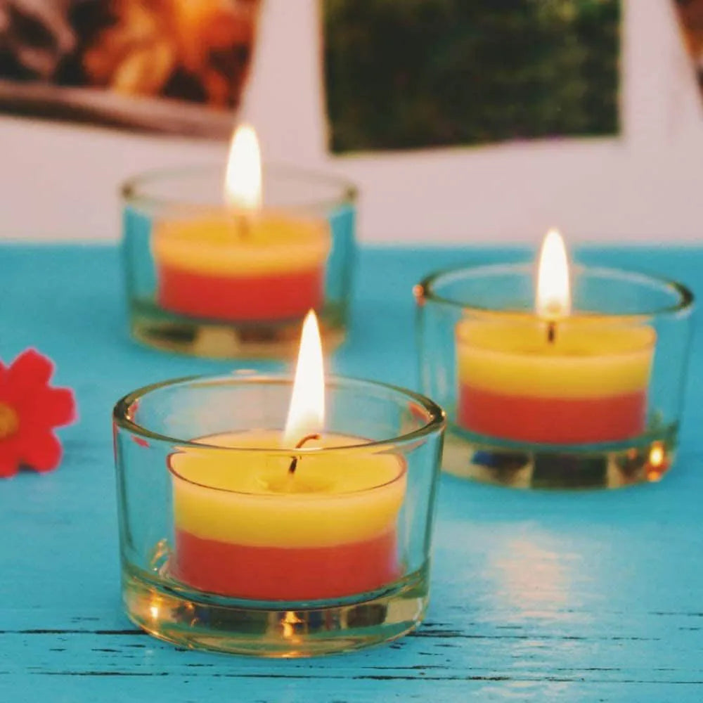 Three clear glass tealight holders with lit candles on a blue table
