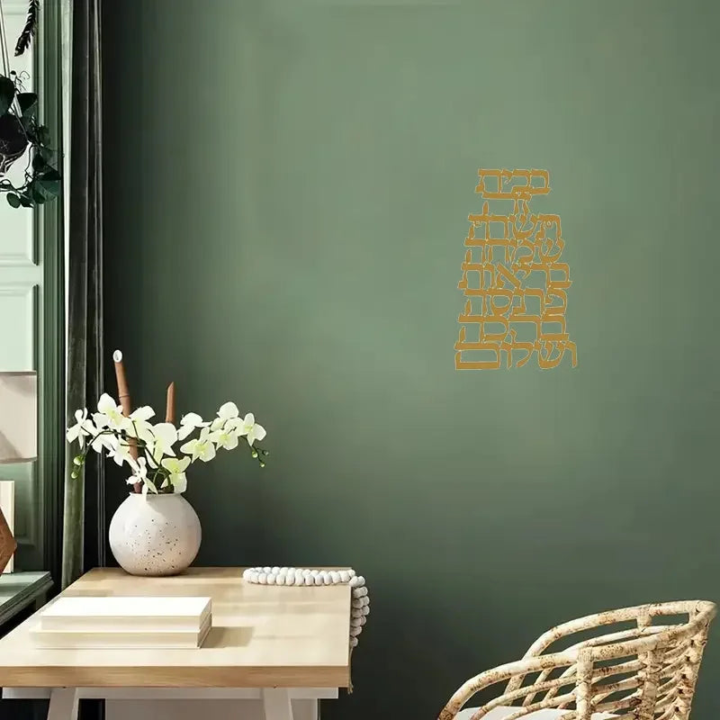 Gold Hebrew script metal wall art shown above a desk in a cozy home office with green wall