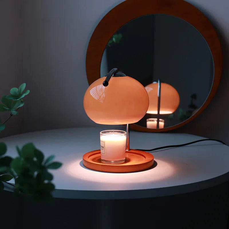 Glass candle warmer lamp glowing on a bedside table with jar candle, mirror in background