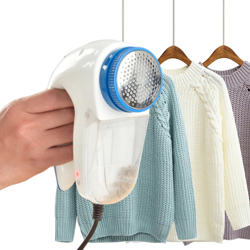 Hand holding plug-in electric lint remover with sweaters in background