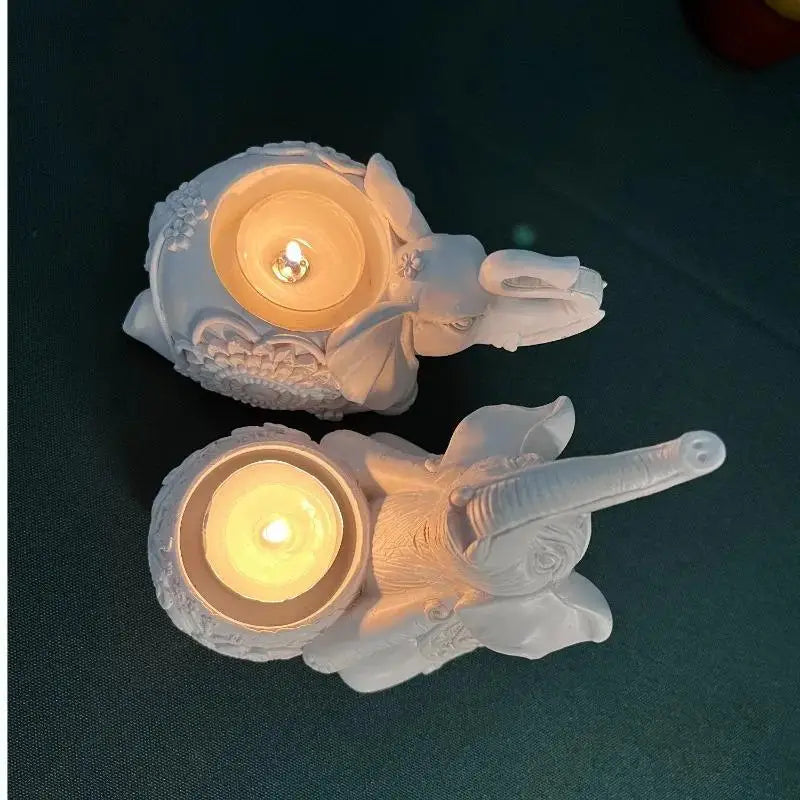 Top view of two white resin elephant tealight holders with lit tealight candles inside, on a green surface.