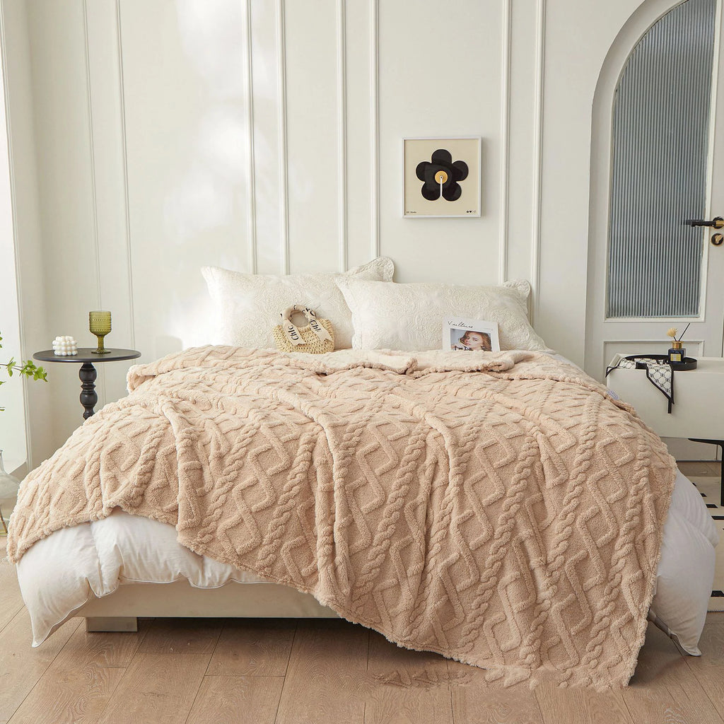 Braided sherpa fleece throw blanket spread out on a made bed in a bright bedroom