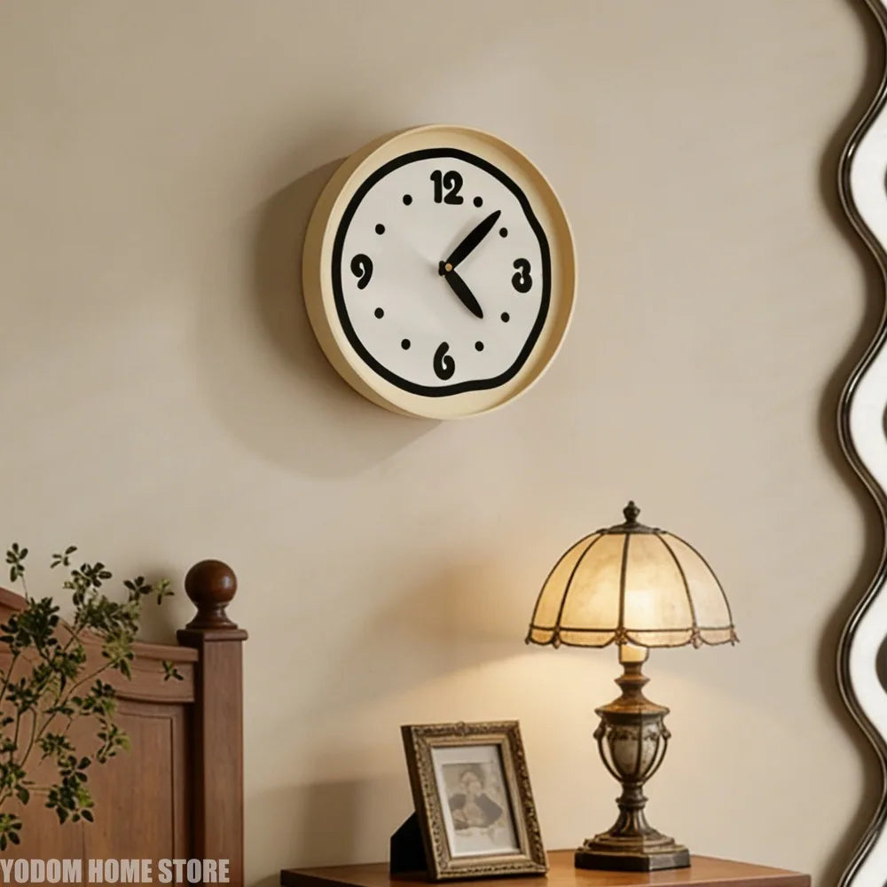 Cream round wall clock with black edge displayed above a wooden nightstand with lamp in bedroom