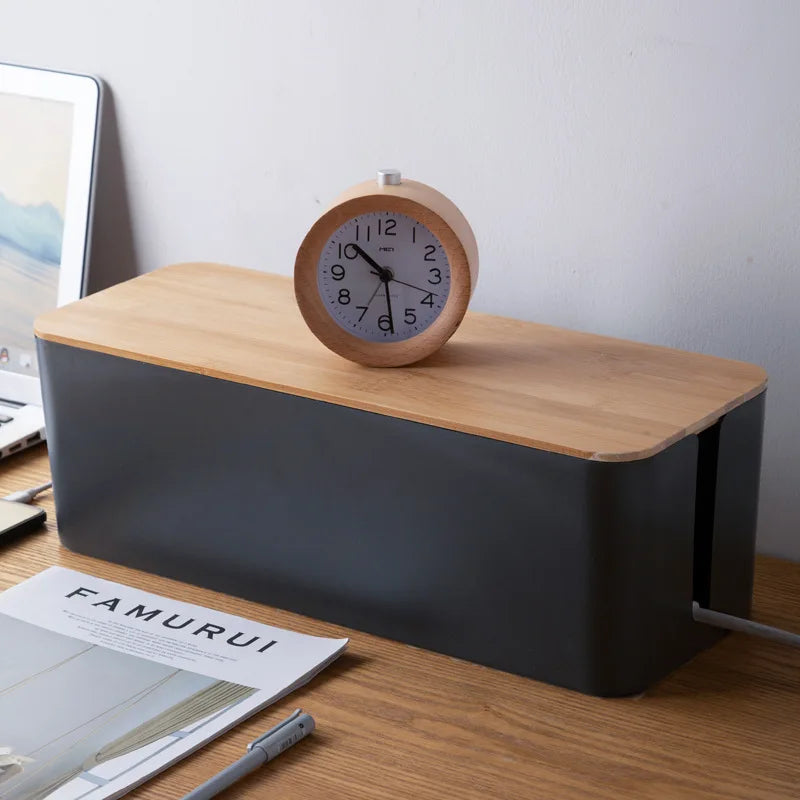 Black cable box with bamboo lid on a desk, clock on the lid