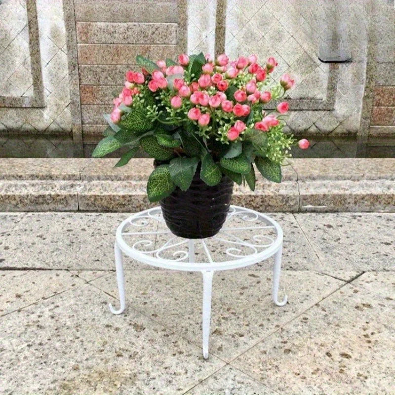 White round metal plant stand with decorative scrollwork holding potted flowers outdoors