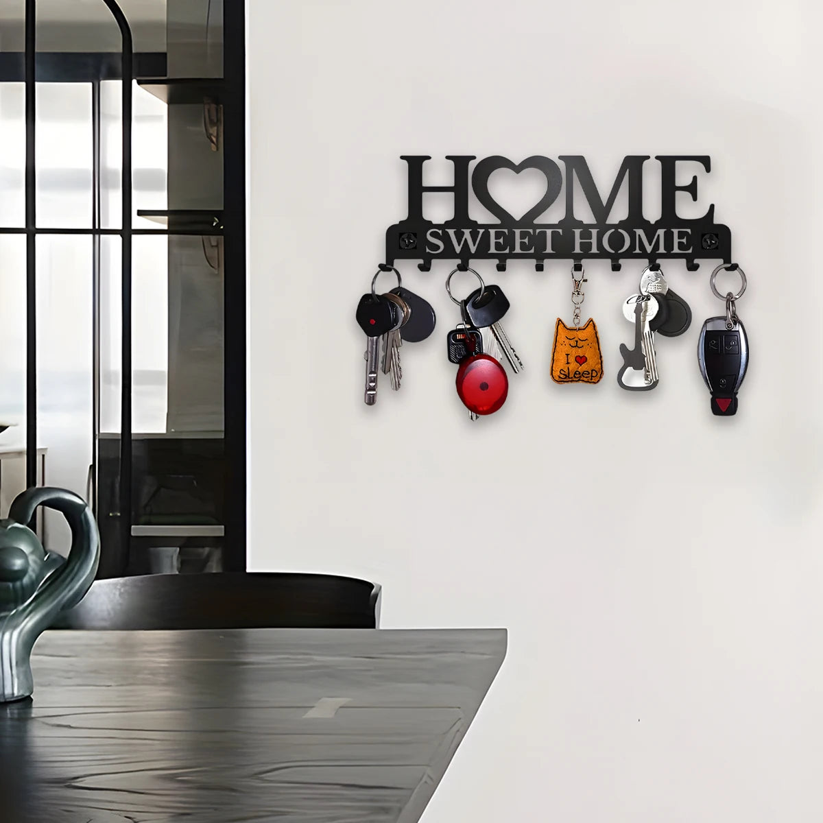 Wall-mounted black metal key rack with 10 hooks in use near a dining area, holding several sets of keys.