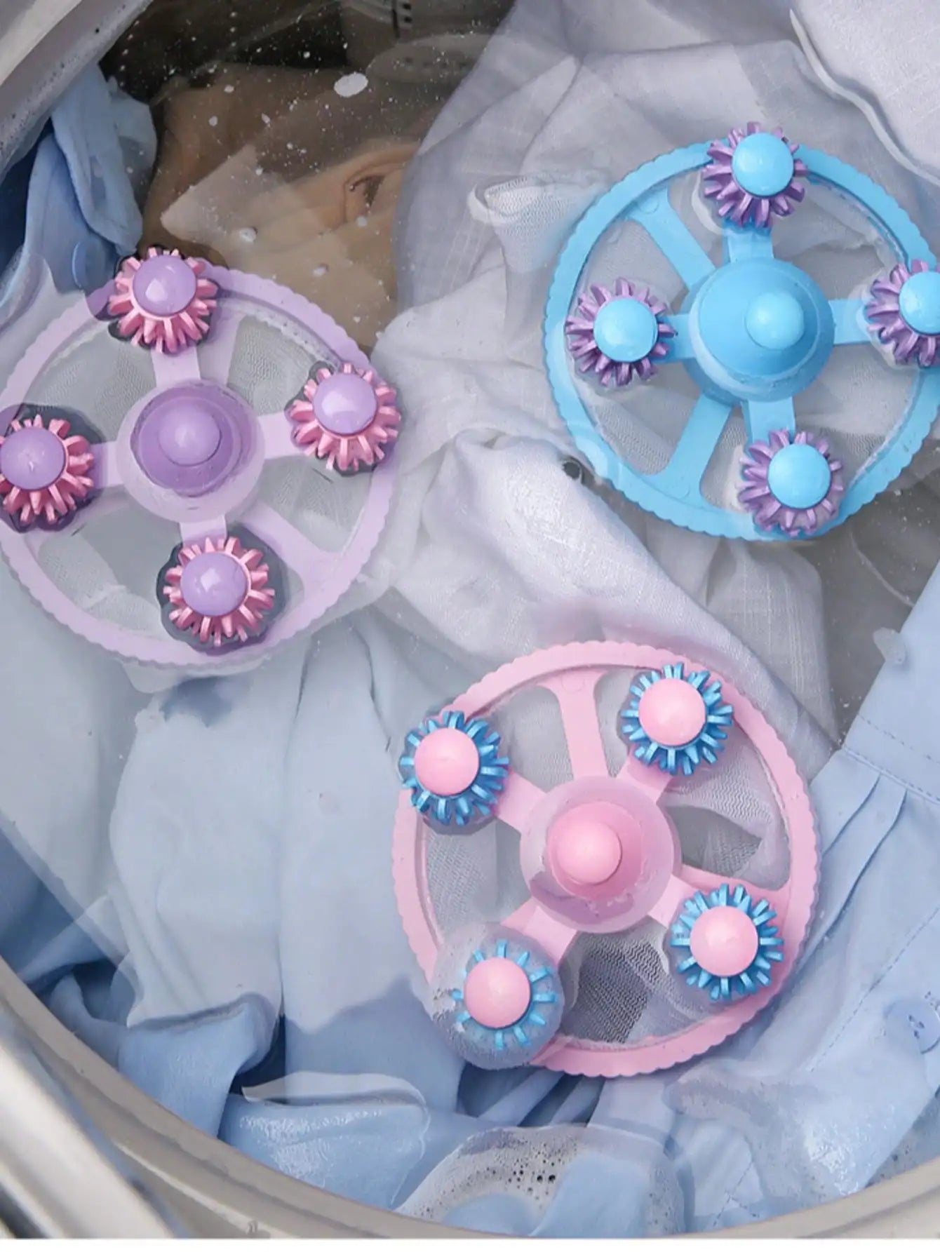 Three floating lint catcher balls in blue, pink, and purple colors inside a washing machine with laundry