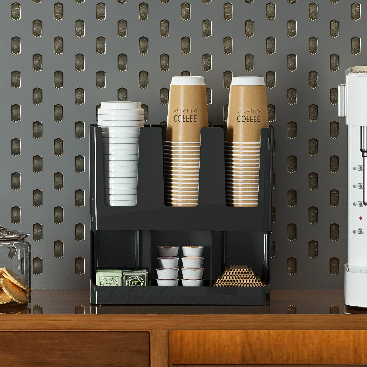 Coffee bar organizer in black plastic for home or office, displayed on a wood counter against a patterned wall, neatly filled with coffee essentials.