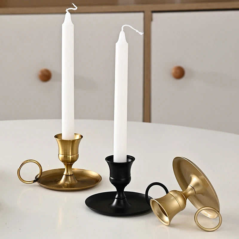Two chamberstick candle holders—one gold, one black—each with taper candles, and a third gold holder lying on its side