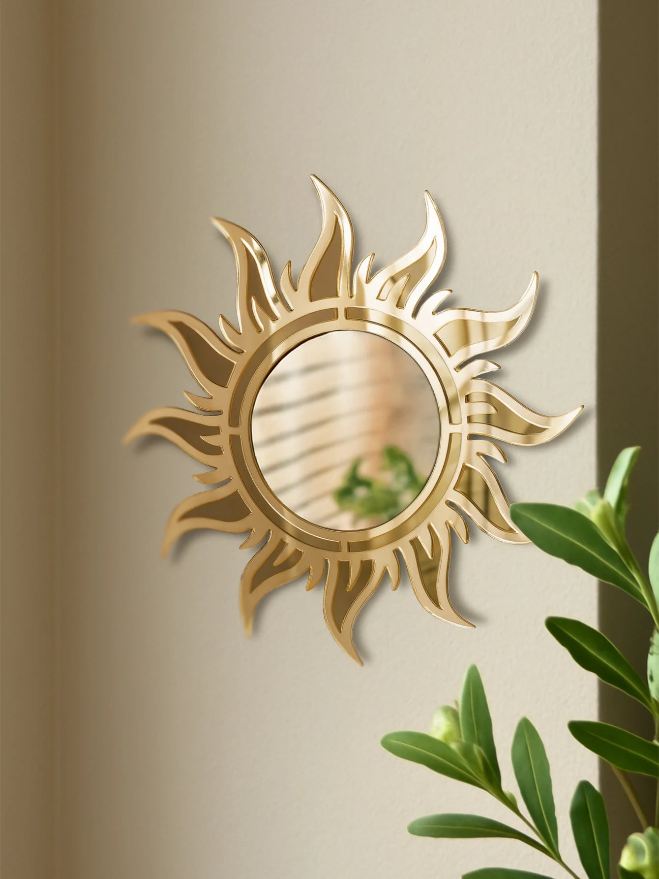 Acrylic sunburst wall mirror with gold finish styled on a neutral wall above green plants