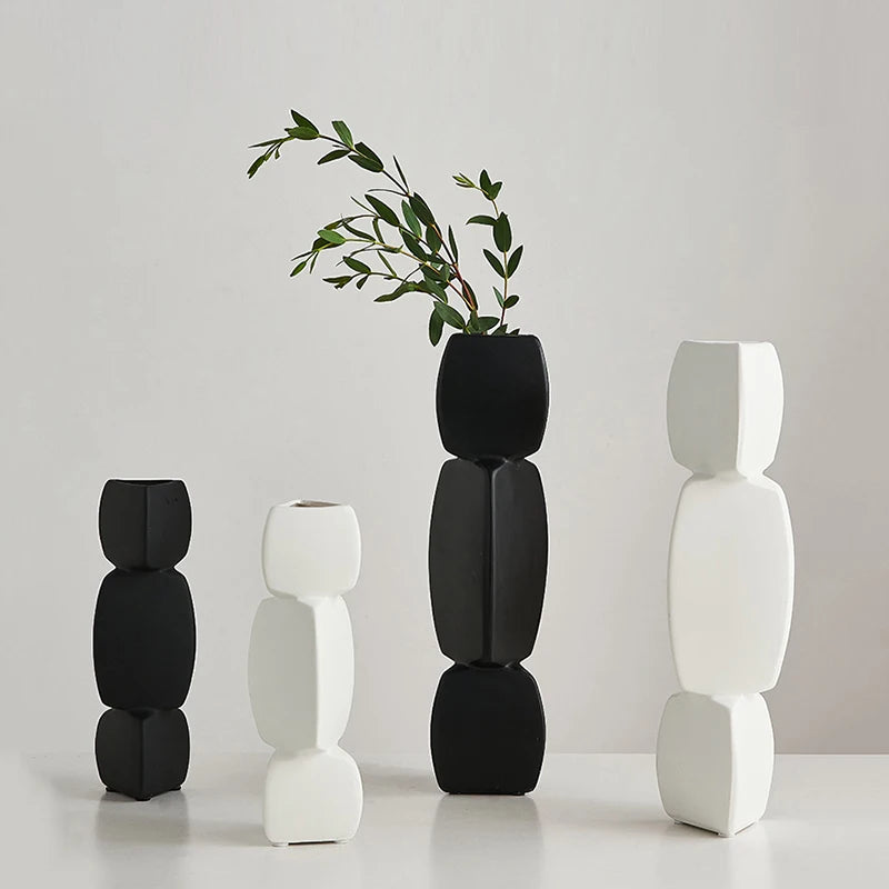 Four sculptural ceramic vases in black and white on a tabletop, modern stacked shapes