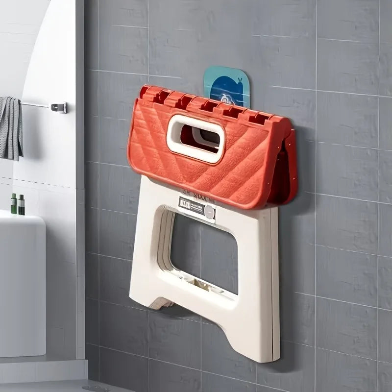 red folding step stool shown folded and hanging on a bathroom wall hook