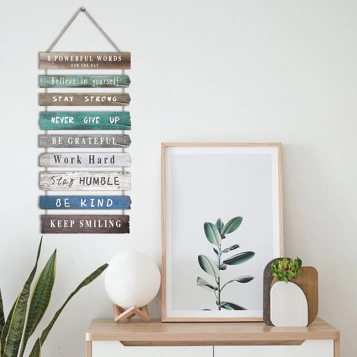 Wooden multi-color motivational wall art above a sideboard with framed plant print and decor accents