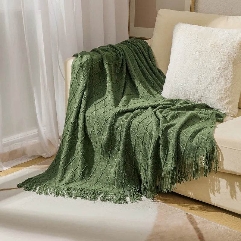 Green knit throw blanket with tassel fringe draped on a beige sofa