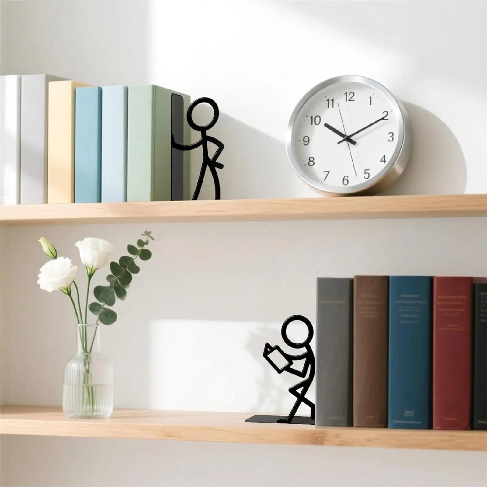 Stick figure bookends placed on a light wood shelf with books, a clock, and a vase