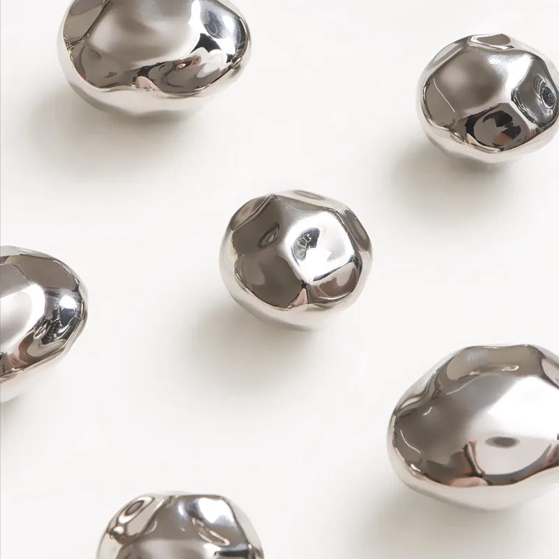 Close-up of several hammered silver stone-shaped wall hooks on a light background