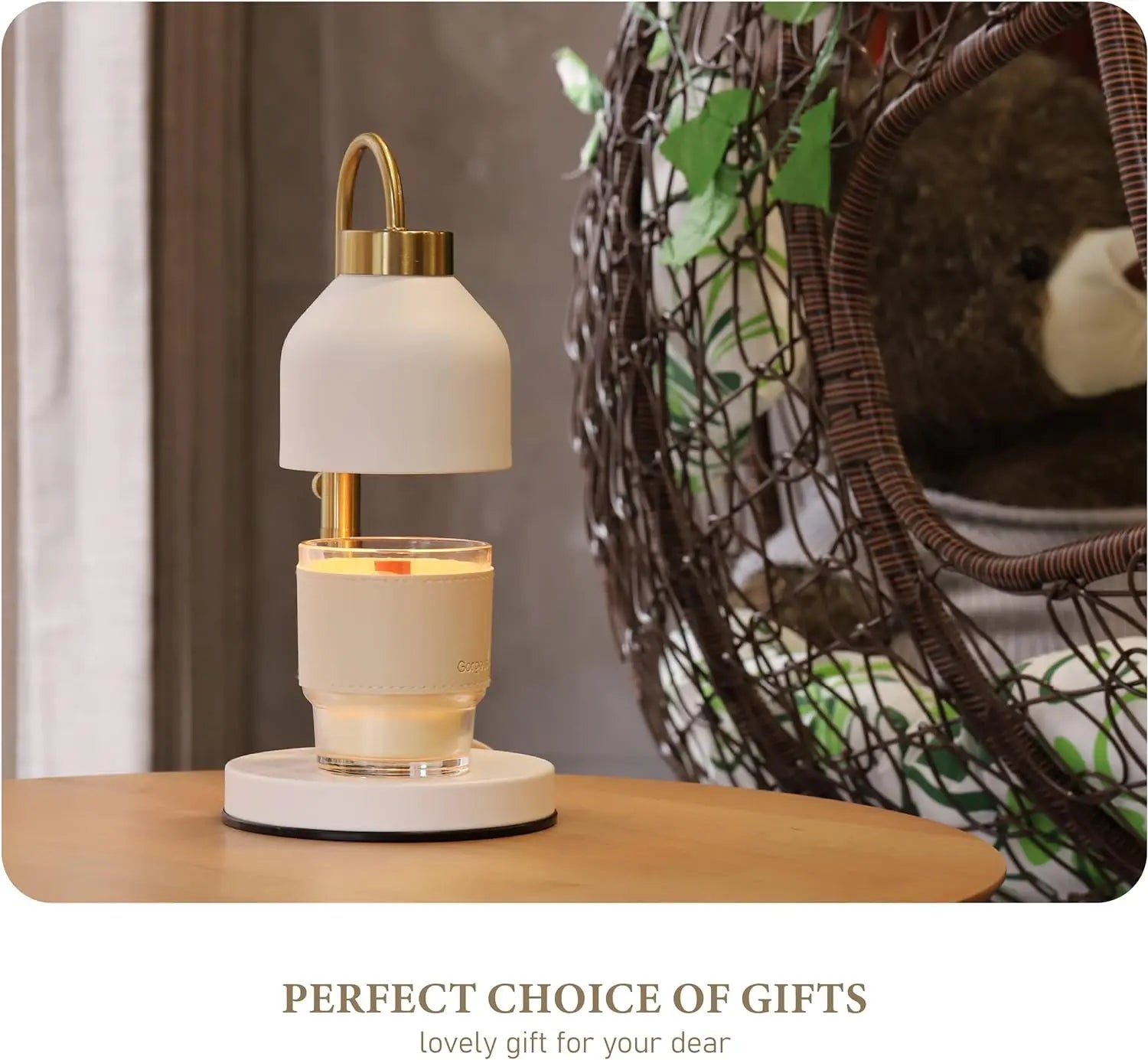 White candle warmer lamp on a table with a lit candle in a glass jar, next to a woven hanging chair