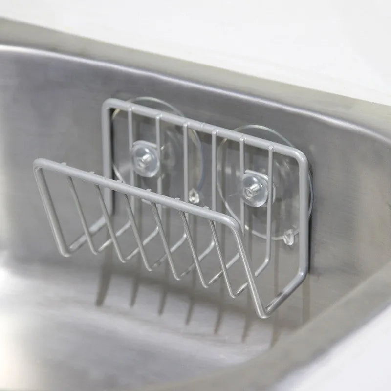 Silver stainless steel sponge caddy attached with suction cups to a kitchen sink wall
