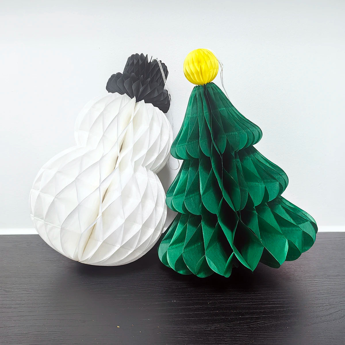 Close-up of honeycomb paper snowman and green Christmas tree ornaments on black tabletop