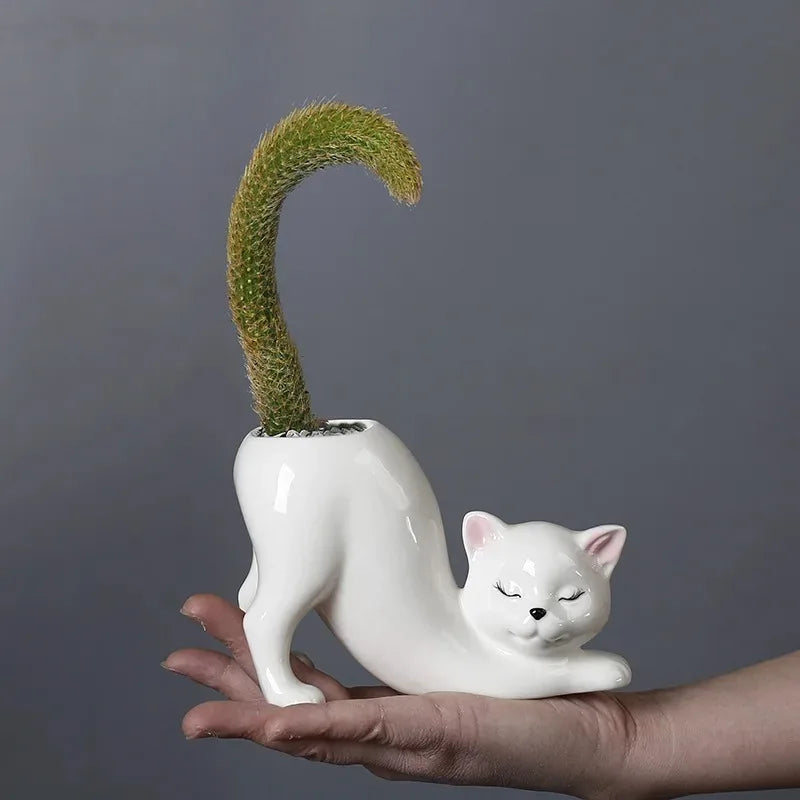 Hand holding a white cat-shaped ceramic planter with a cactus, showing scale
