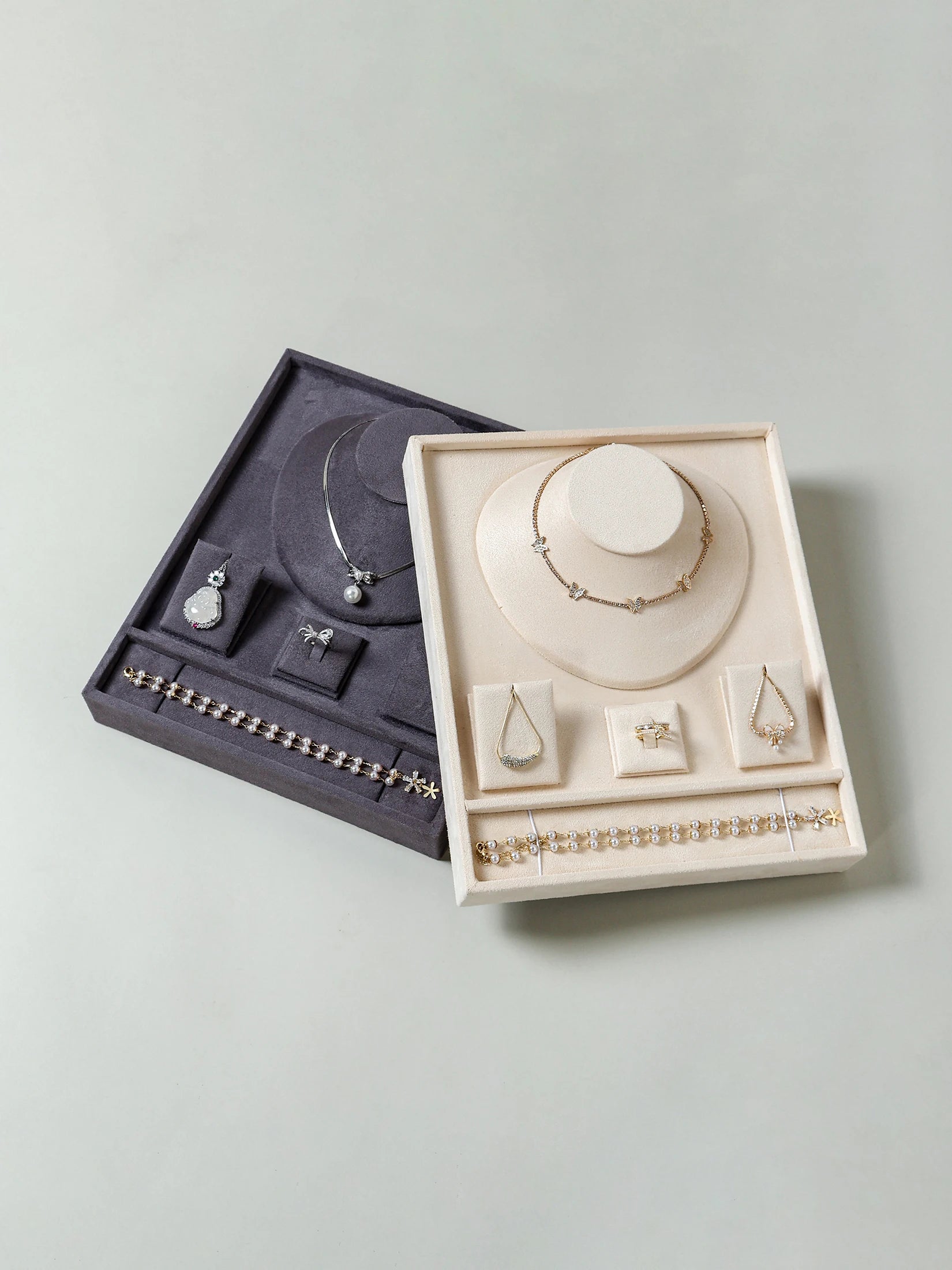 Partitioned beige and gray velvet jewelry trays with space for rings, bracelets, and necklaces on a flat surface