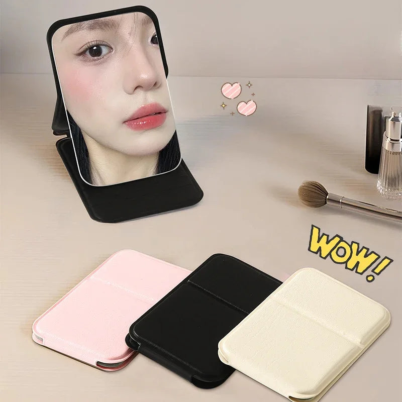 Black foldable PU leather makeup mirror standing open on a vanity, with pink and beige closed mirrors beside it