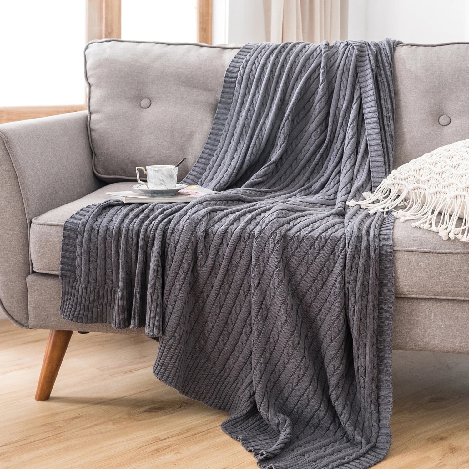 dark grey cable knit cotton throw blanket draped over a grey sofa in a living room