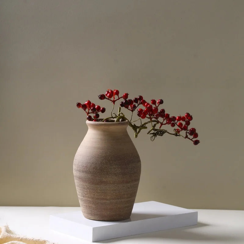 Rough clay ceramic vase on white platform with dried red berry stems