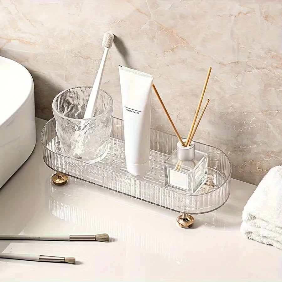 Clear acrylic vanity tray with gold feet holding a toothbrush cup, toothpaste, and diffuser on a bathroom counter