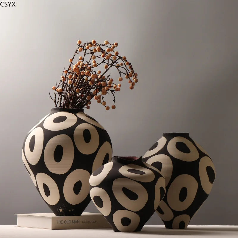 three geometric ceramic vases, one with dried botanicals arranged inside, displayed on a table