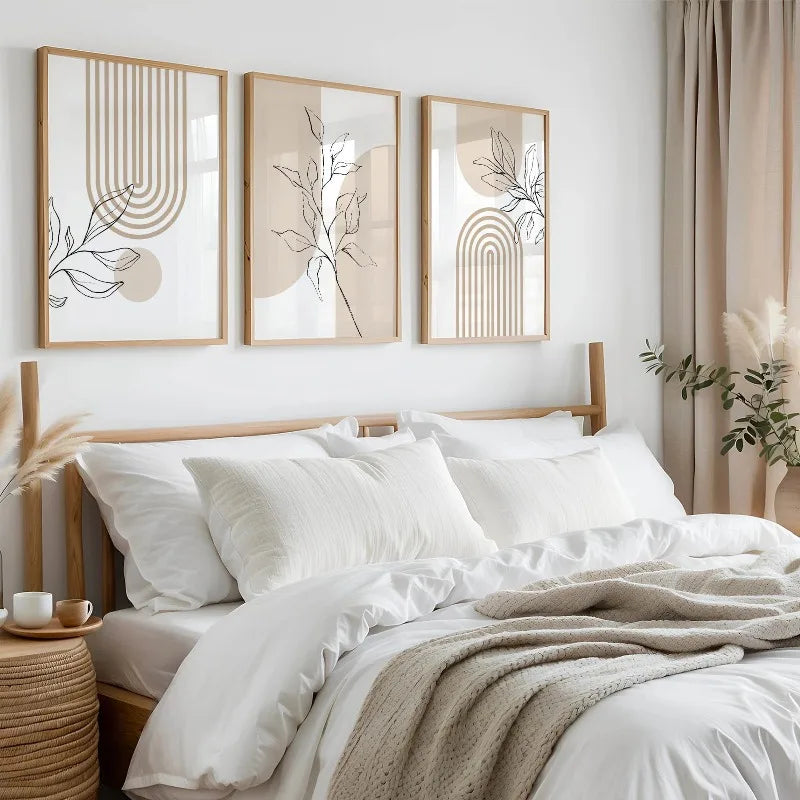 Neutral botanical wall art trio framed and hung over a made bed in a softly lit minimalist bedroom